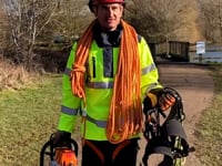 Innovation II Smock Hi-Vis Yellow worn by a tree surgeon holding chainsaws and climbing gear outdoors.