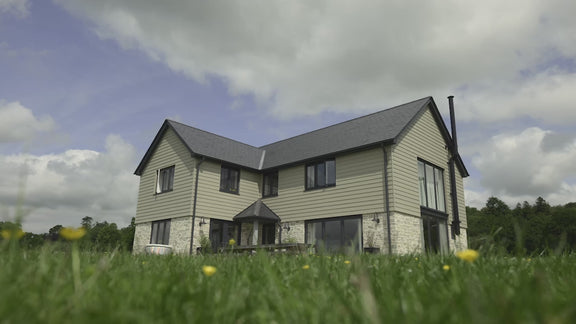 Modern two-story house with a lush green lawn and cloudy sky in the background.