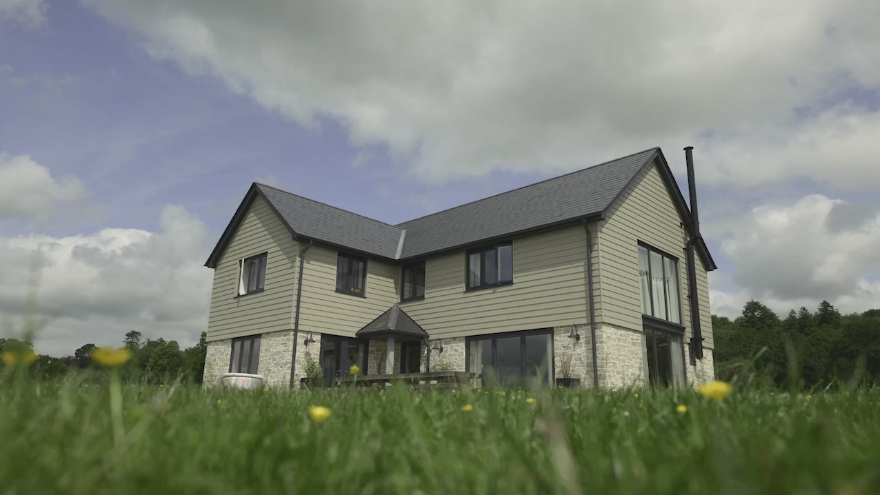 Modern two-story house with a lush green lawn and cloudy sky in the background.