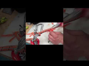 Close-up of a climber's hand working with orange climbing rope and carabiner on a workbench.