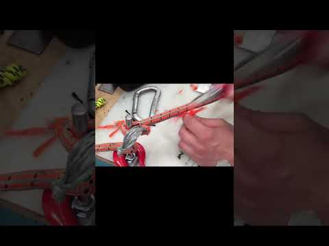 Close-up of a climber's hand working with orange climbing rope and carabiner on a workbench.
