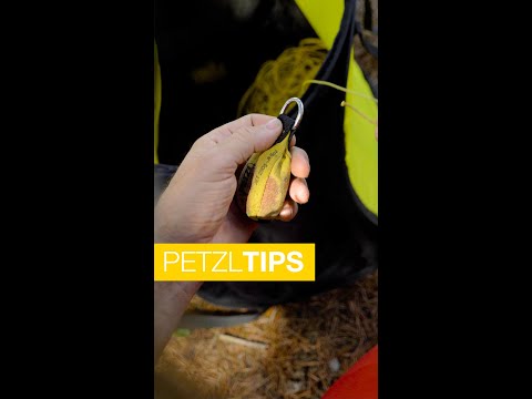 Hand holding PETZL throw-line pulley, designed for tree surgeons and arborists, with visible yellow rope and gear.