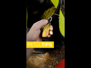 Hand holding PETZL throw-line pulley, designed for tree surgeons and arborists, with visible yellow rope and gear.