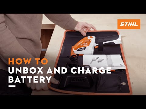 User demonstrating how to unbox and charge STIHL cordless tool battery with instructional manual.