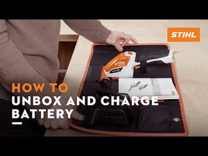 User demonstrating how to unbox and charge STIHL cordless tool battery with instructional manual.
