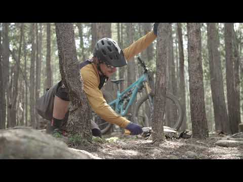 A cyclist using a Gomboy Curve Folding Saw to clear branches on a mountain biking trail among trees.