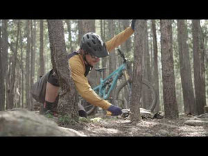 A cyclist using a Gomboy Curve Folding Saw to clear branches on a mountain biking trail among trees.