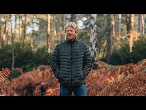 Man wearing a warm, lightweight green reversible puffer jacket in a forest setting, perfect for tree surgeons.