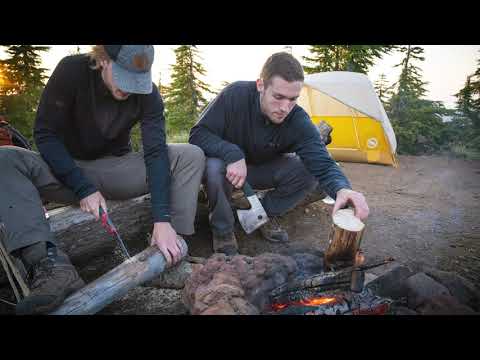 Two campers using a F180 Handsaw Replacement Blade Fine Teeth for wood cutting by a campfire.