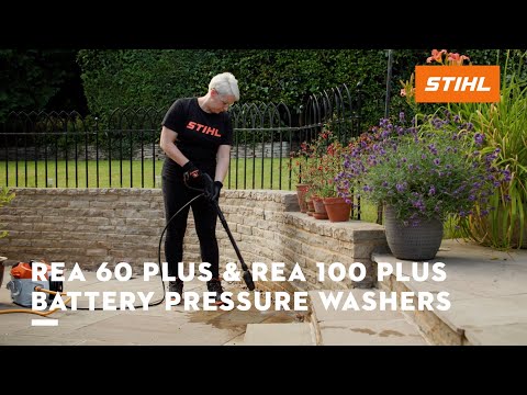Person using REA 60 PLUS Cordless Pressure Washer on patio with flowers and garden in the background.