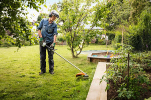 Man using STIHL FS 56 RC-E Petrol Brushcutter in a garden for efficient grass mowing and maintenance.